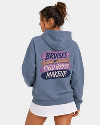 Woman wearing a blue hoodie with text bruises are field hocley makeup standing against a plain background