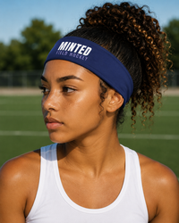 Woman wearing a blue headband with 'Minted Field Hockey' text on a turf field.